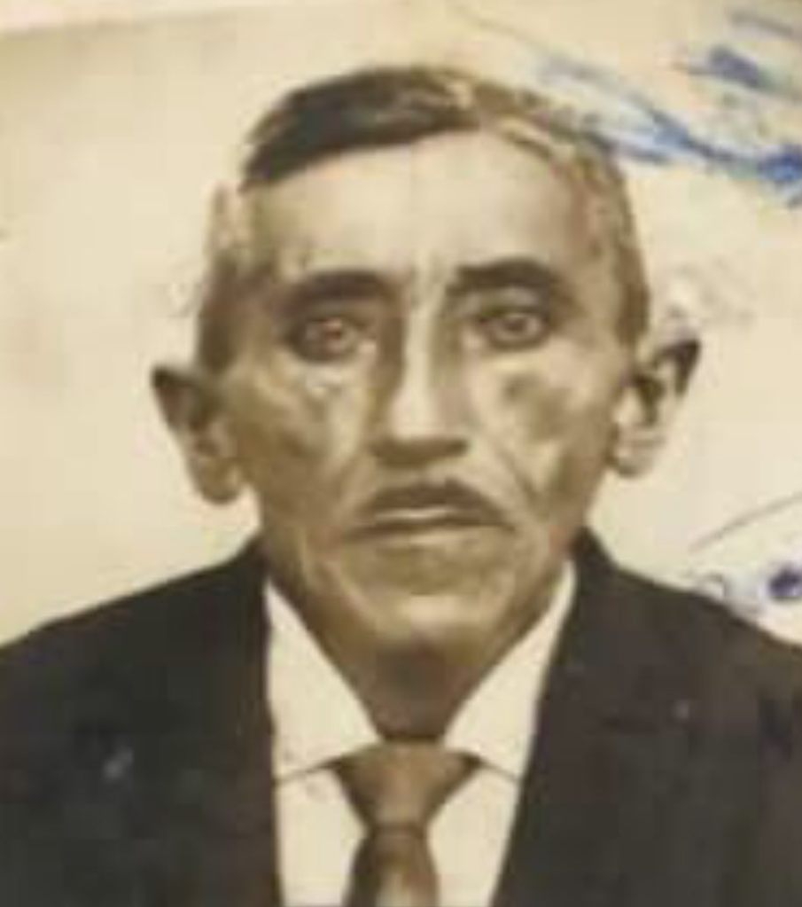 Retrato antigo em preto e branco de Mariano Belarmino. Ele é um homem de meia-idade, com cabelos escuros penteados para o lado, bigode fino e olhos claros e expressivos. Veste um traje formal composto por paletó escuro, camisa branca e gravata. A foto apresenta marcas do tempo e pequenas manchas azuladas no canto superior.